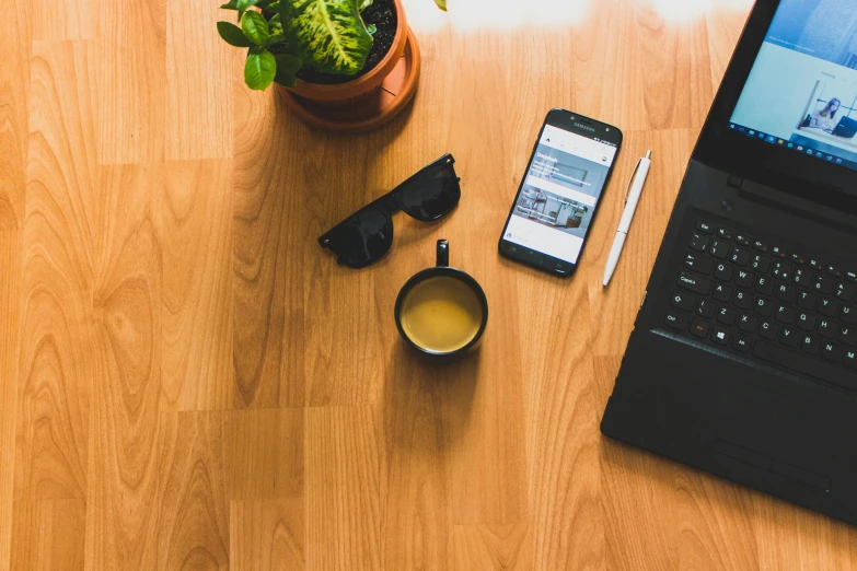 a table topped with a laptop and phone next to a cup