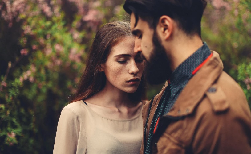 a woman standing next to a man by some trees