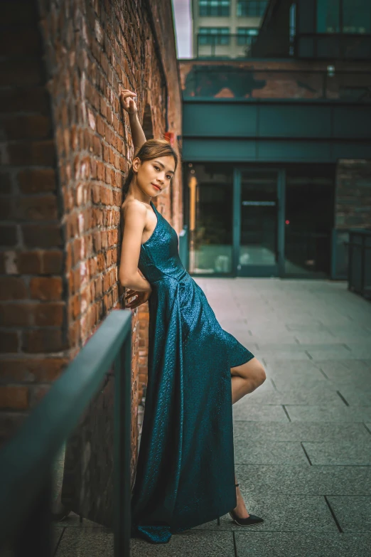 a young woman in a long dress leans against a brick wall on a street