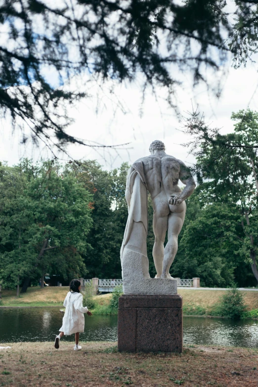 a woman is standing near a statue in the park