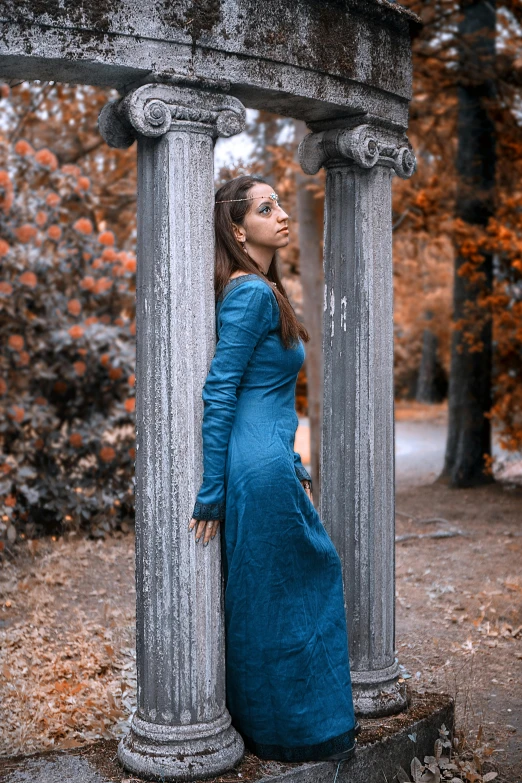 woman in blue dress leans against pillars in wooded area