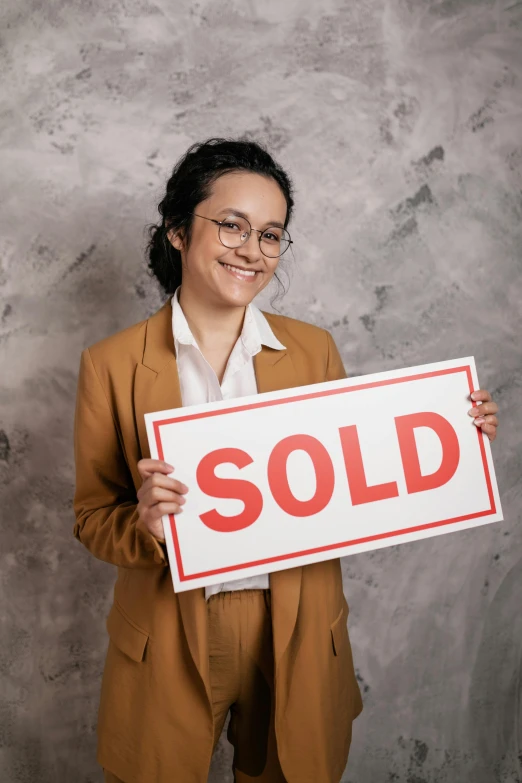 a young woman holding up a sold sign with her right hand