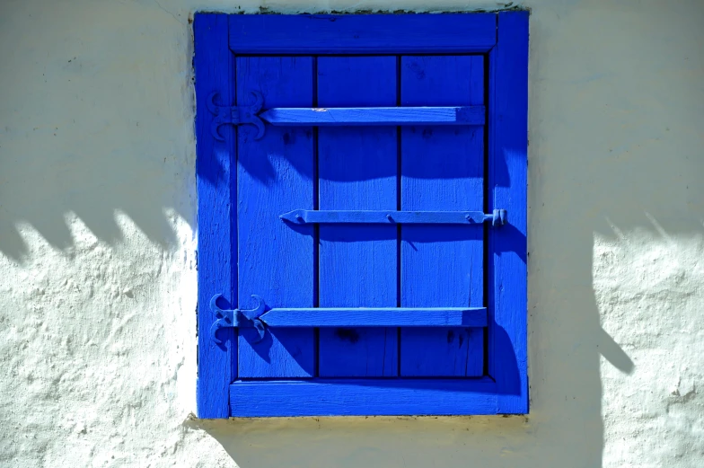 the small blue window has a wooden shutter and shelf on it