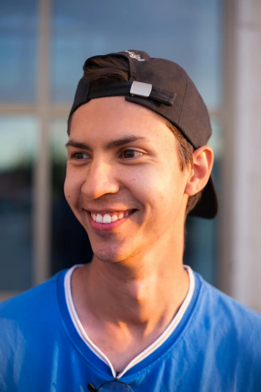 a man is smiling while wearing a blue shirt and black hat