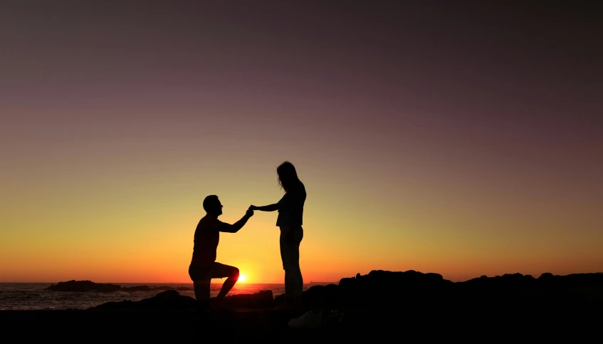 a couple holding hands with the sun setting in the background