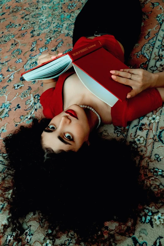 a woman laying on the floor holding a red book