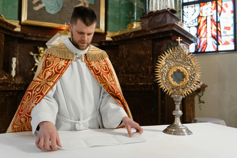 a priest sitting at a table with his hands near an object on top