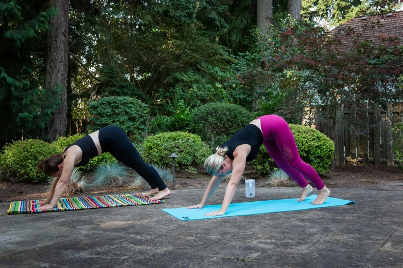 two women performing yoga outdoors with towels on the ground