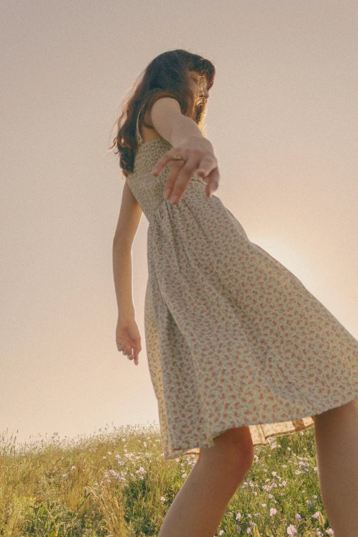 a woman walking through a grass field with her dress blowing in the wind