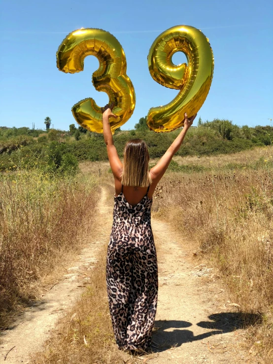 the woman is walking down a dirt path and holding up two balloons