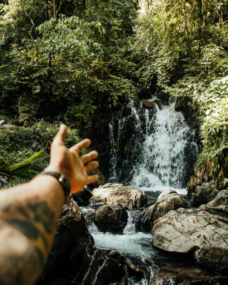 a man with his hand up near a waterfall