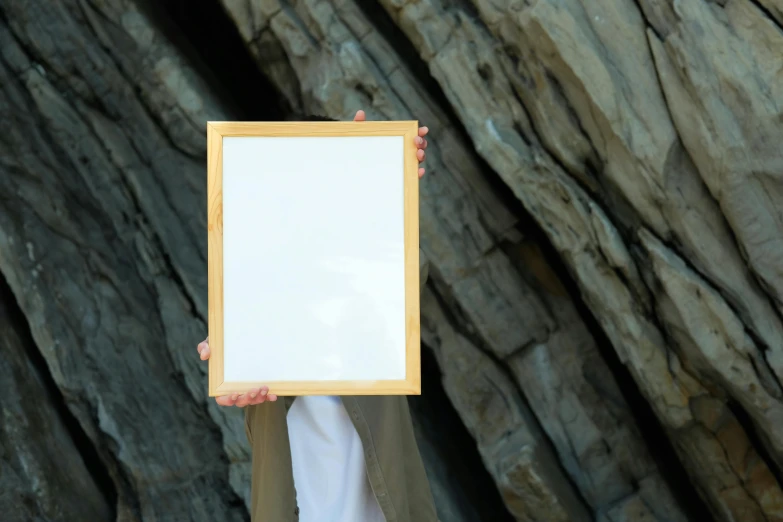 a person holds a white square sign in front of a mountain