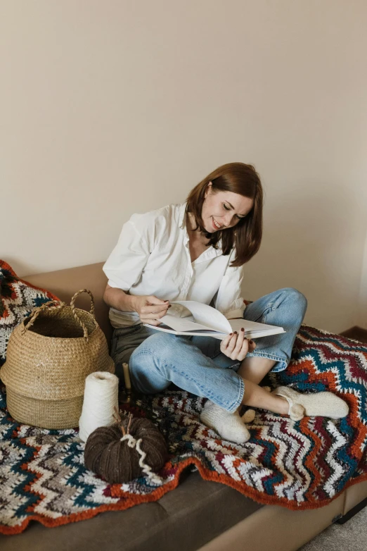 a woman sits on a bed, reading a book and knitting