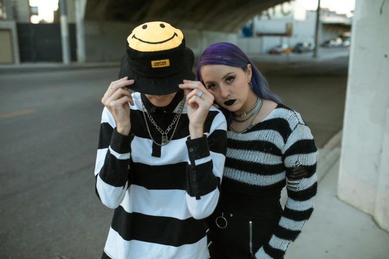 two women in sweaters, one with a smiley face cap on