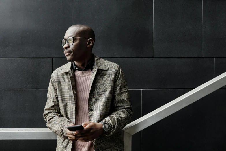 a smiling man with eyeglasses holding a cellphone next to a railing