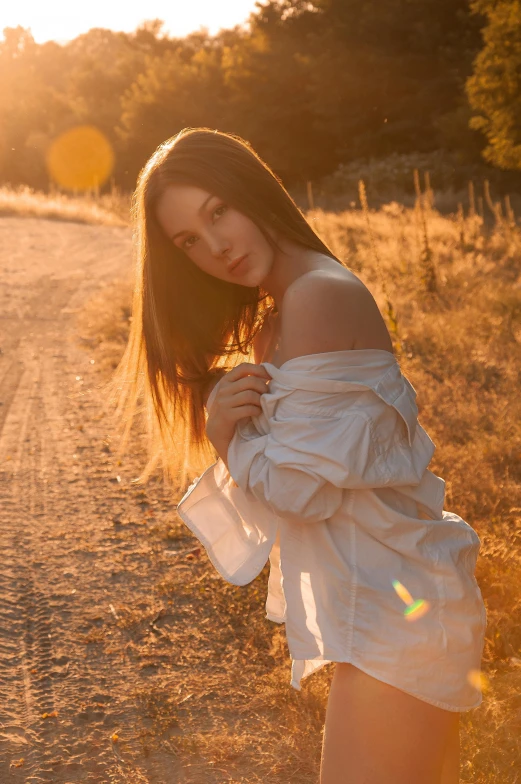 an attractive young woman standing on a dirt road near the sunset