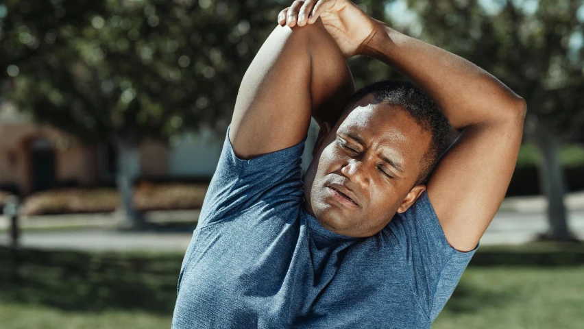 man stretching in the sun with his hands behind his head