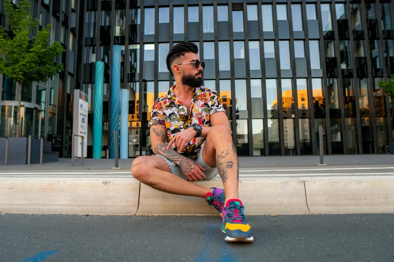 a man sits on the side of a curb while wearing a colorful shirt