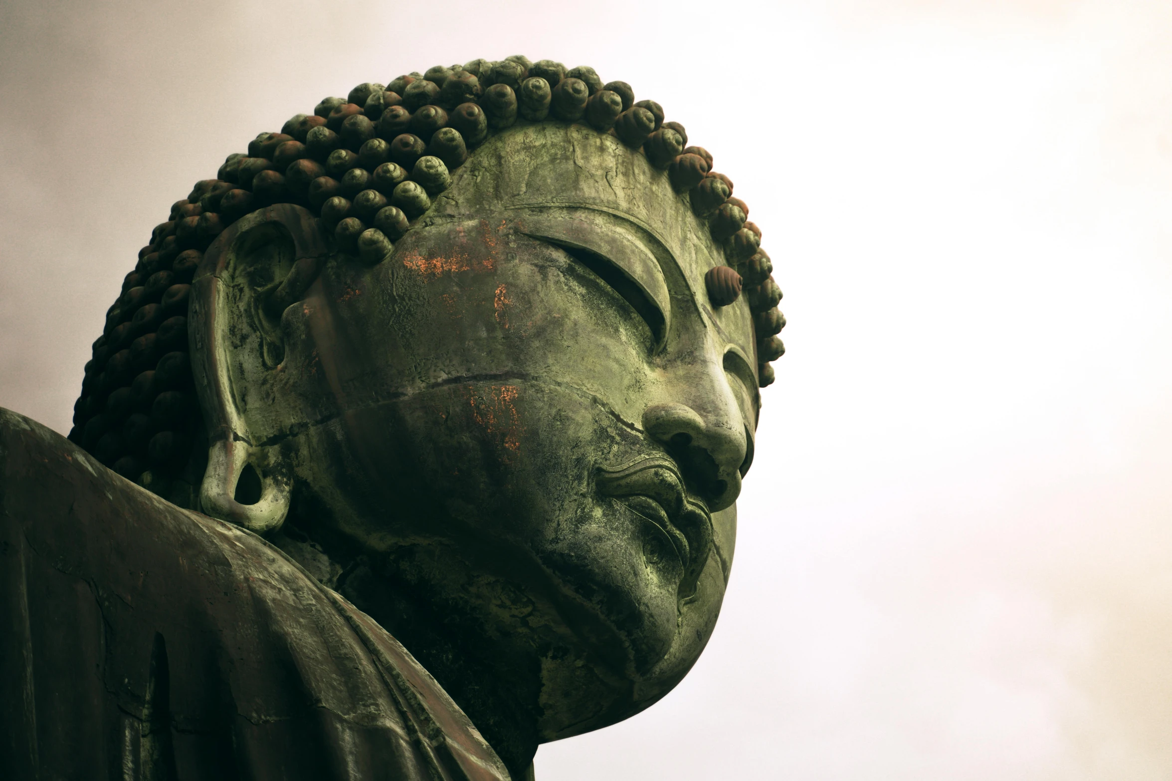 a green buddha statue head with its eyes closed