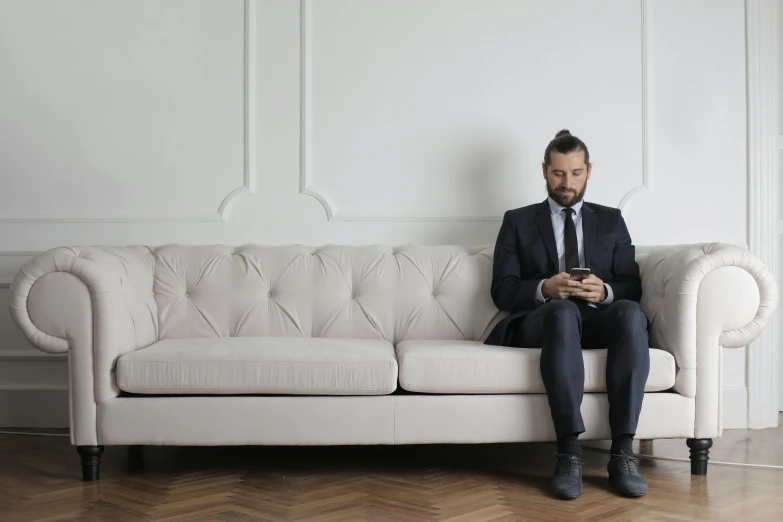 the man is sitting on the couch while checking his cell phone