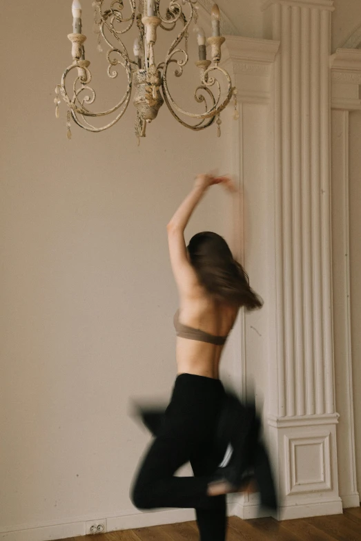 a woman in black dance pants in front of a chandelier