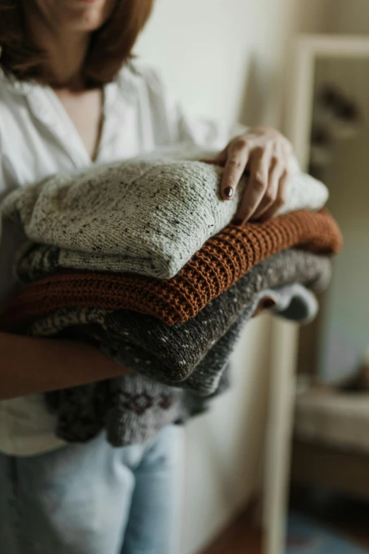 a woman carrying a large pile of folded sweaters