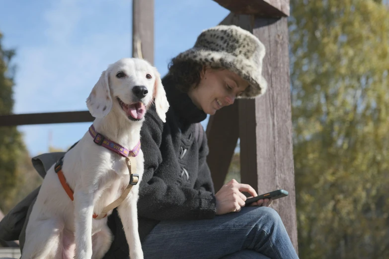 a woman sitting with a dog using her cellphone