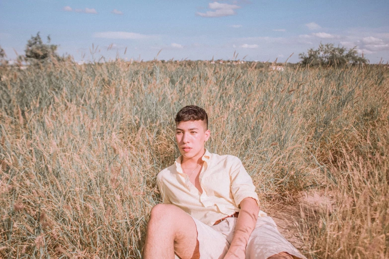 a man wearing a short white shirt sitting in a field