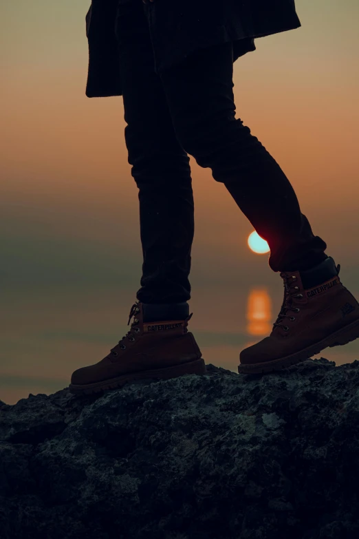 man wearing brown hiking boots standing on rocky outcropping