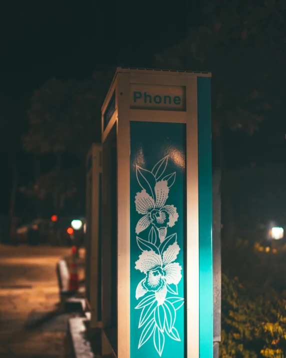 a phone booth with flowers drawn on it at night