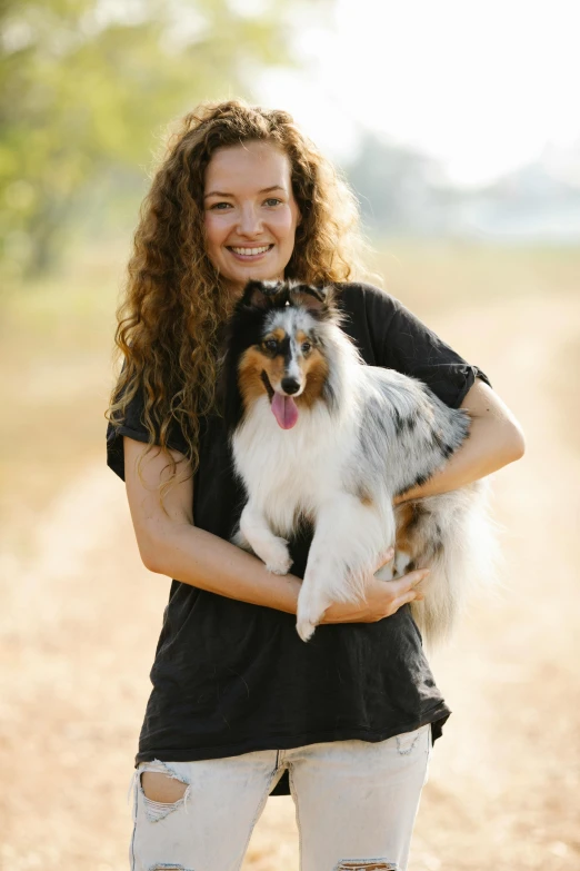 a woman with long curly hair holds her dog in a field