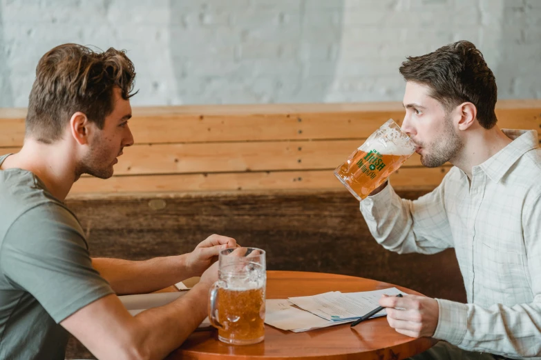 two men sitting at a table with beer in their hands