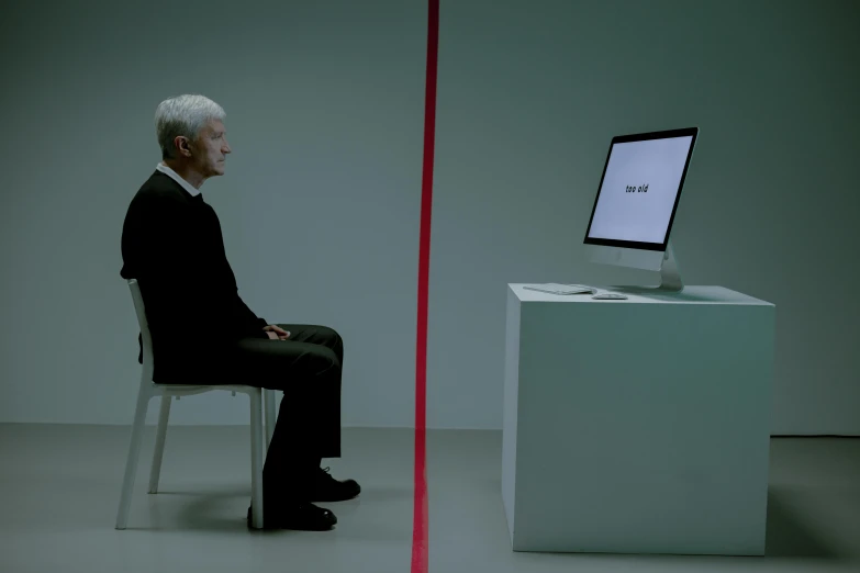 a man sitting in a chair, watching an apple computer on a desk