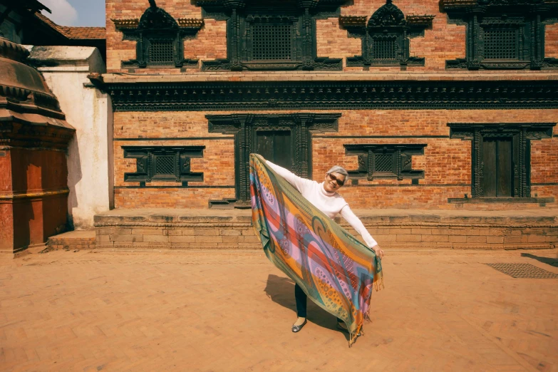 woman carrying colorful blanket in front of large brick building