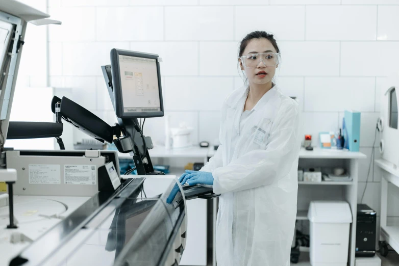 a woman in white lab coat standing near monitor