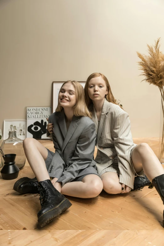 two beautiful young women sitting on top of a wooden floor