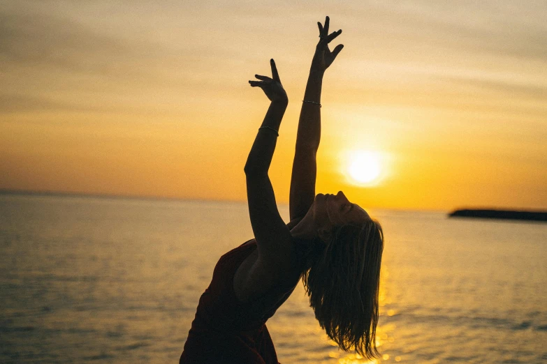 a woman is standing up in front of the sunset, and reaching her hands to catch a frisbee