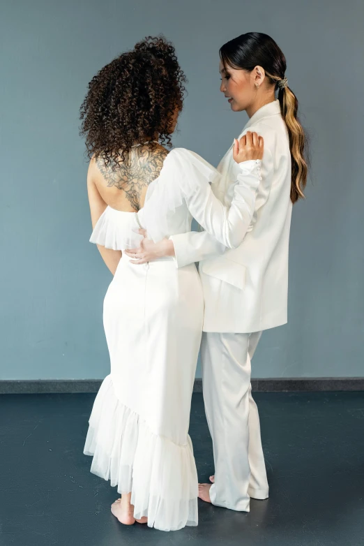 two girls in white clothing dancing against a grey wall