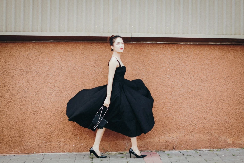 a young woman with a large black dress is walking down a sidewalk