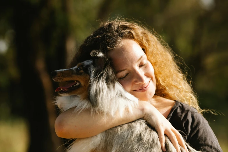 a woman hugging a dog outdoors while the dog looks down at her