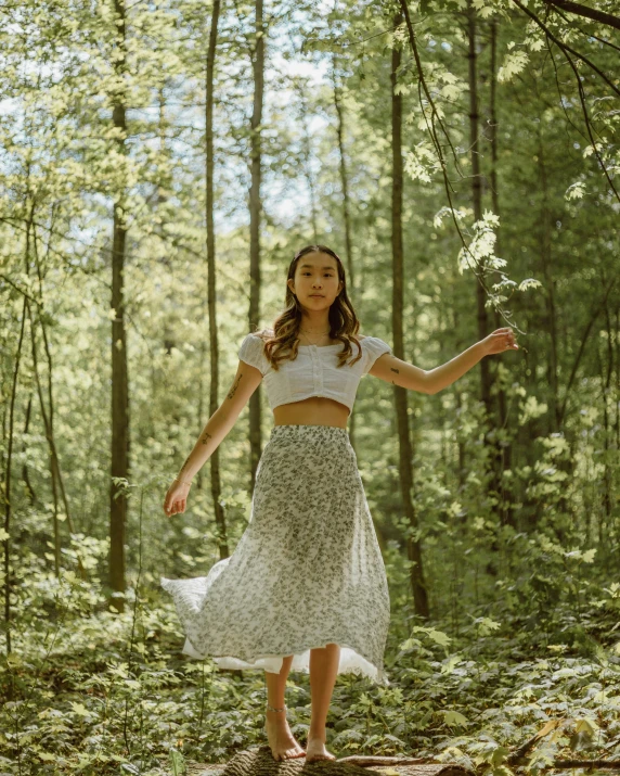 a woman in white and green dress holding a plant in a wooded area