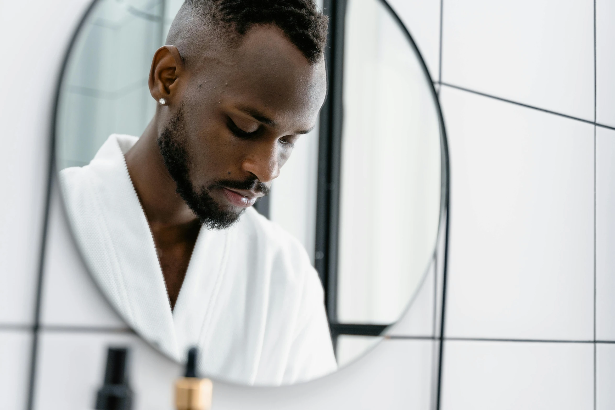 a man with black hair and a towel over his shoulder is in a bathroom mirror