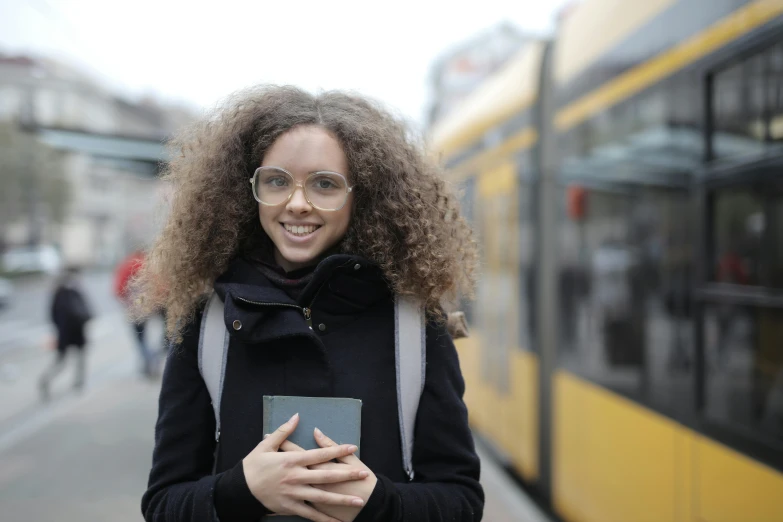 a woman holding a book standing next to a bus