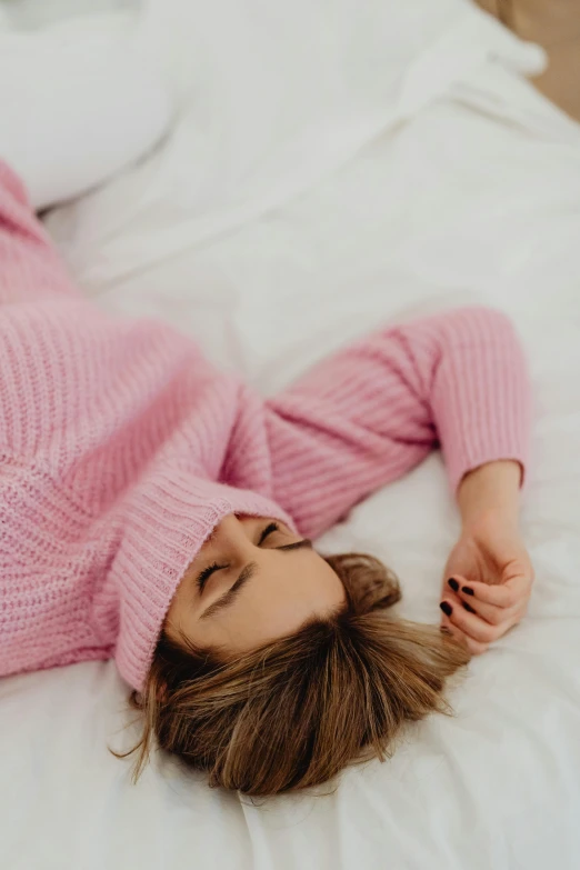 a young woman is laying down on the bed in a pink sweater