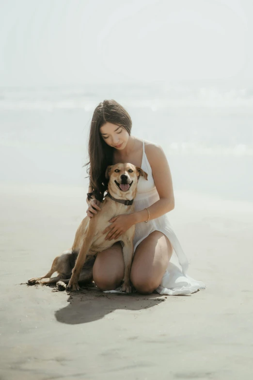 a young woman sitting on the sand next to a dog