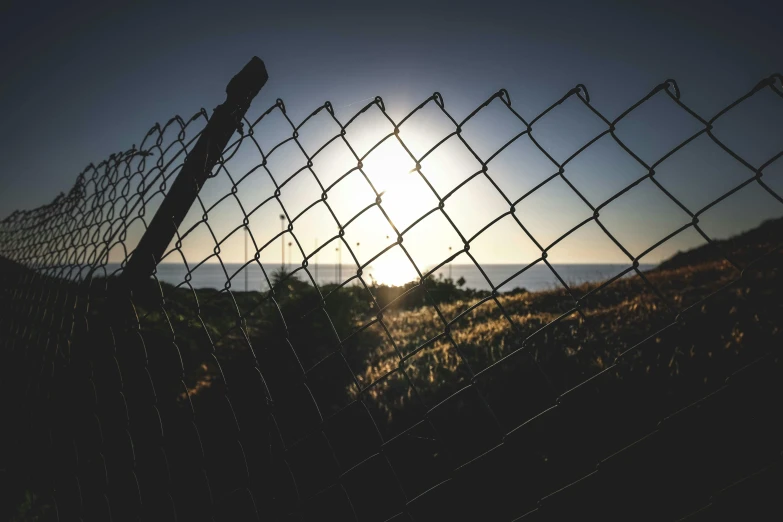 a fence in the grass with the sun setting behind it