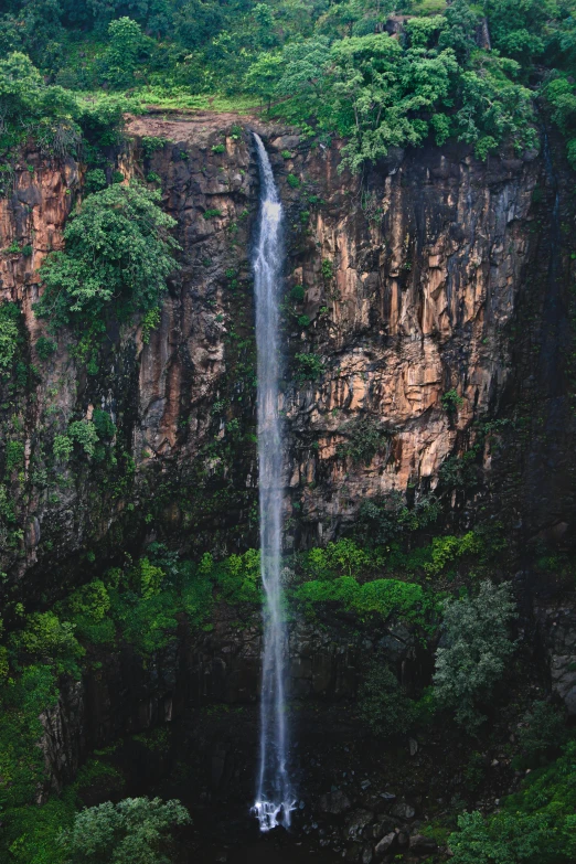 a waterfall near some rocks and green trees