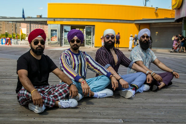 three men with bright colored turbans are sitting on a wooden deck