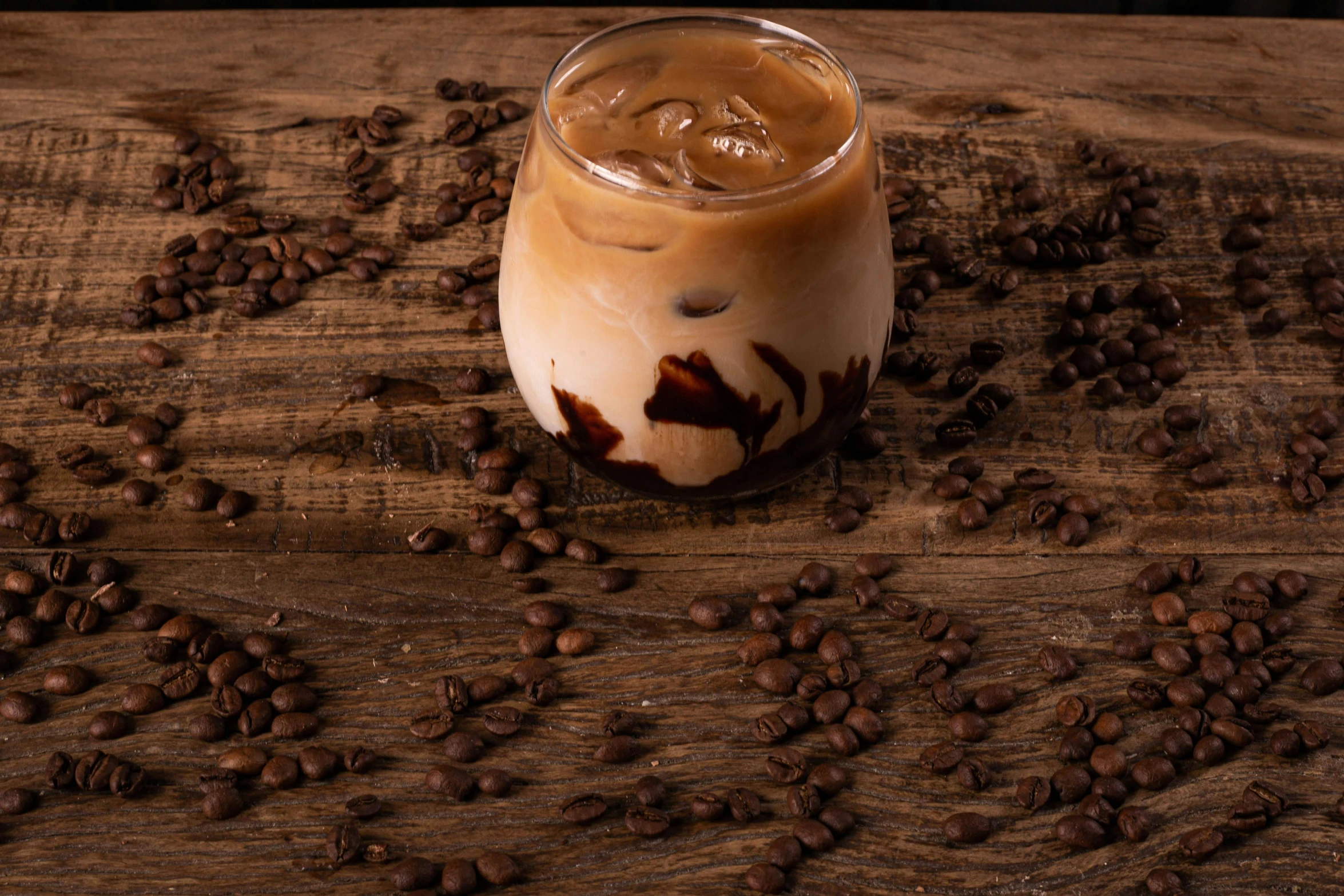 iced coffee on wooden surface surrounded by coffee beans