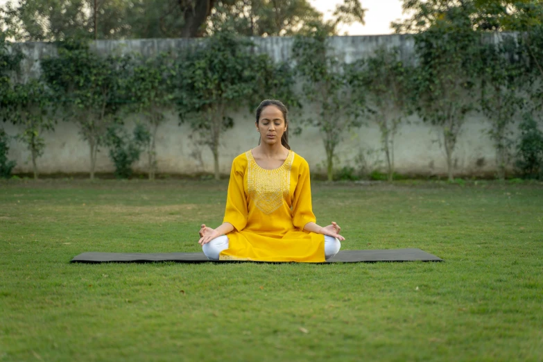 a woman in a yellow top sits in a meditation pose